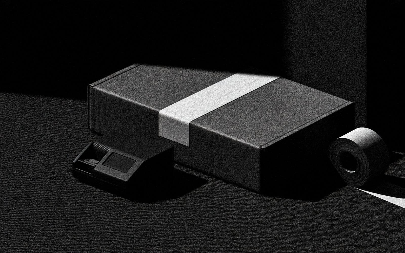 Un colis noir ceint d'un bandeau blanc entre un appareil d'étiquetage et un rouleau, photographie éditoriale sombre en noir et blanc au grain tramé sous une diagonale de lumière.