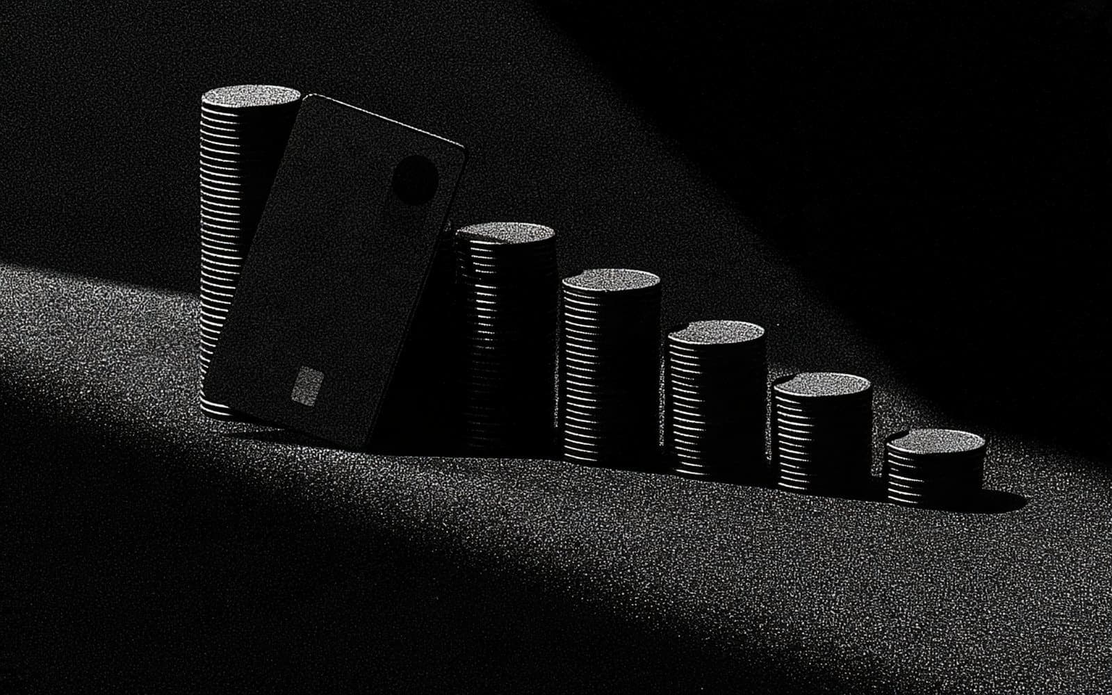 Une carte bancaire appuyée contre des piles de pièces disposées en escalier, photographie éditoriale sombre en noir et blanc au grain tramé sous une lumière directionnelle.