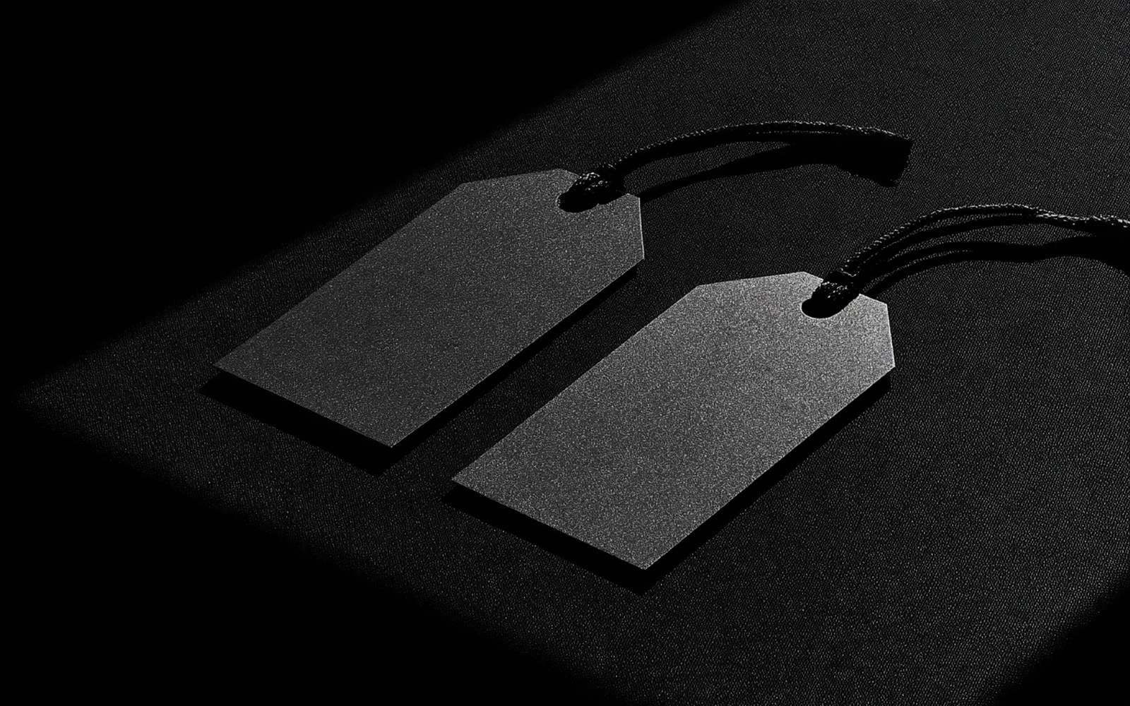 Deux étiquettes de prix sur une surface sombre grainée, photographie éditoriale monochrome avec une diagonale de lumière.